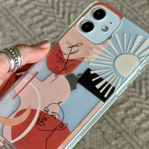 A clear phone case with a minimalist abstract art print, held by a hand with silver rings against a textured beige carpet background. (Feat)