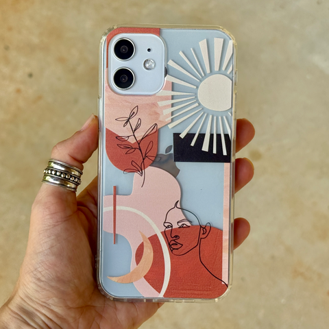 A hand holding a clear phone case featuring a colorful abstract art print with a sun, moon, face line art, and brushstrokes in coral, pink, white, and black. (Feat)