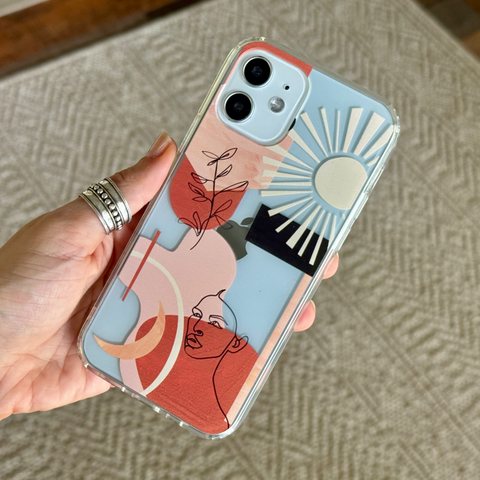 A hand holding a clear phone case with a colorful abstract art print featuring shapes, shown against a textured beige carpet background. (Feat)