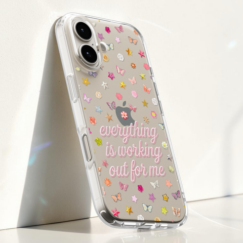 A clear iPhone case with a transparent back, decorated with colorful butterfly and stars and pink script text reading 'everything is working out for me' with a small flower graphic. The Apple logo is visible through the case, indicating compatibility with an Apple iPhone. (Feat)