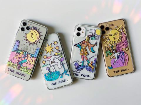 The Moon, The Star, The Fool and The Sun Tarot card designs on clear phone cases. The designs are using pastel colors.
